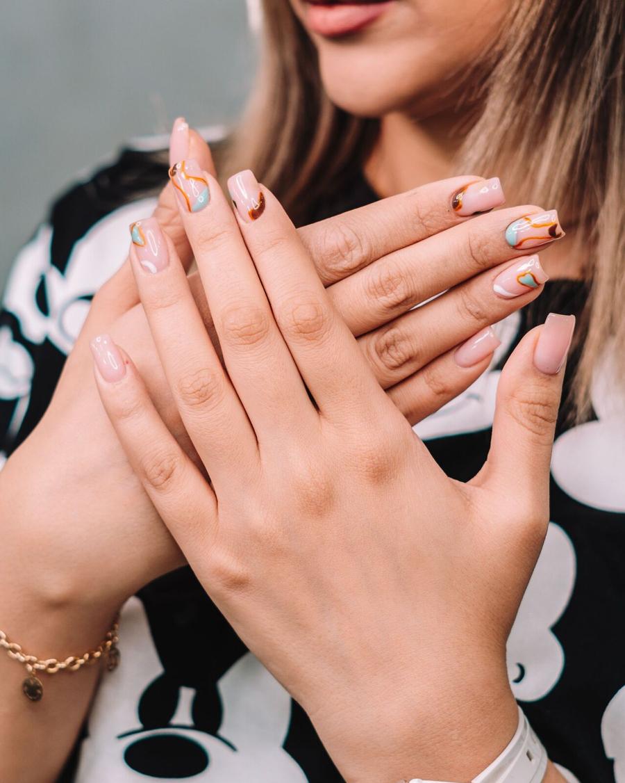 A finished set of nude nails with fine line art, hands crossed at the wrist
