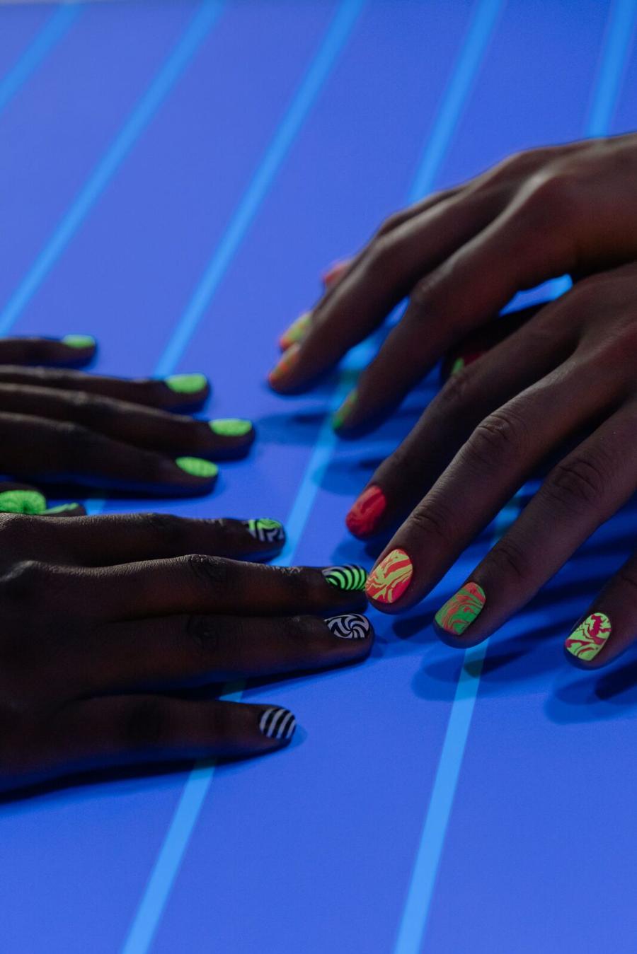 Hands with bright neon nail art under blue studio light