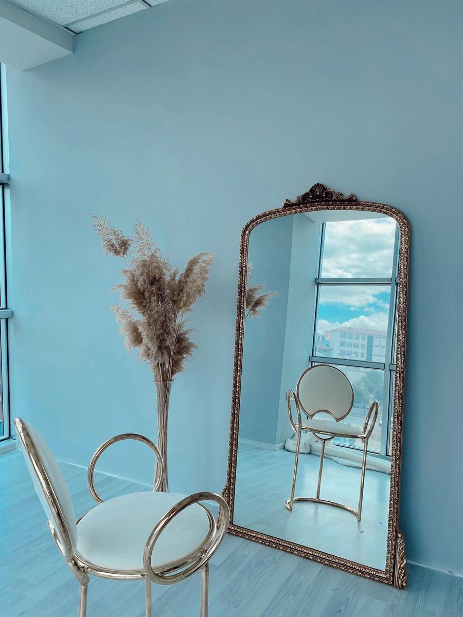 A corner of the studio: pale blue wall, a tall mirror and dried grasses